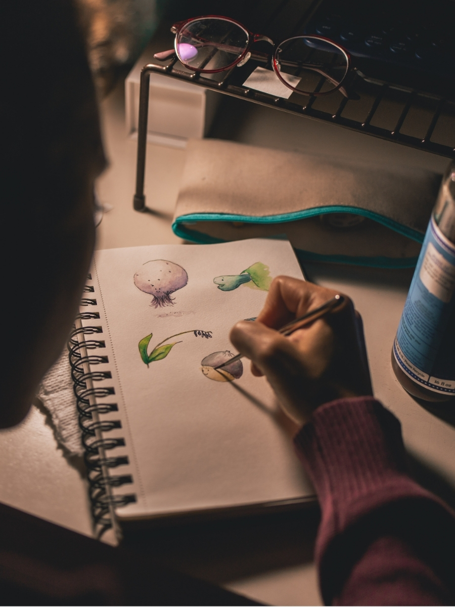 Person sketching colorful botanical illustrations in a notebook