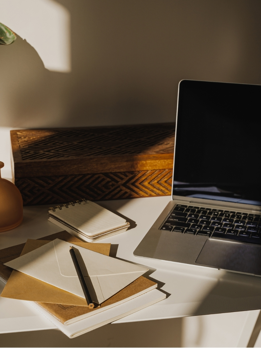 Laptop, notebooks, and stationery arranged on a sunlit workspace
